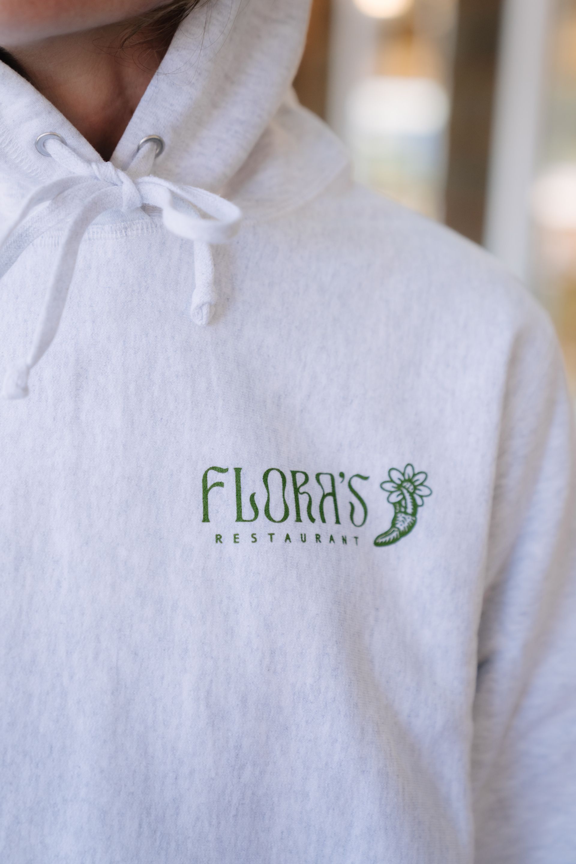 A person wearing a light gray hooded sweatshirt with a green 