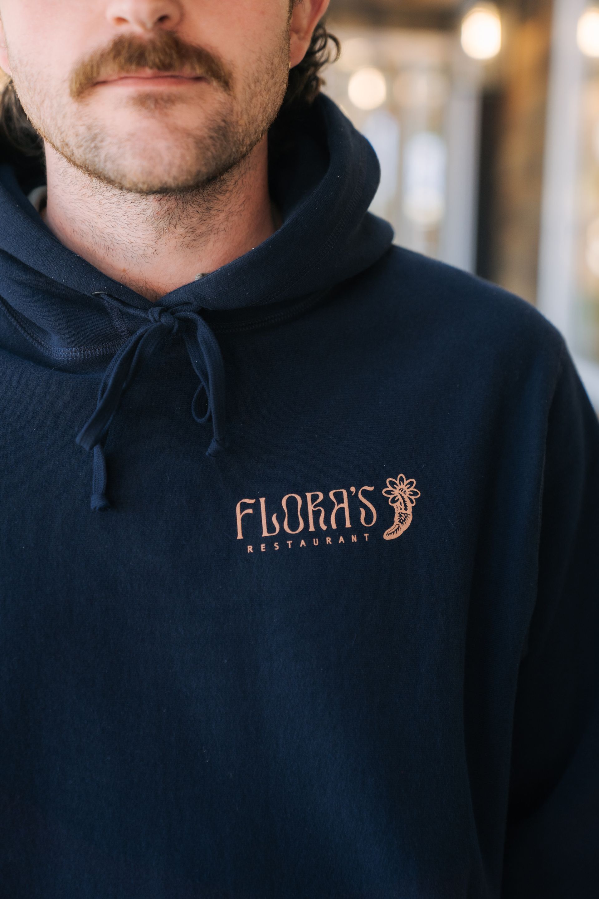 A person with a mustache wearing a navy blue hoodie featuring the copper-colored logo for 