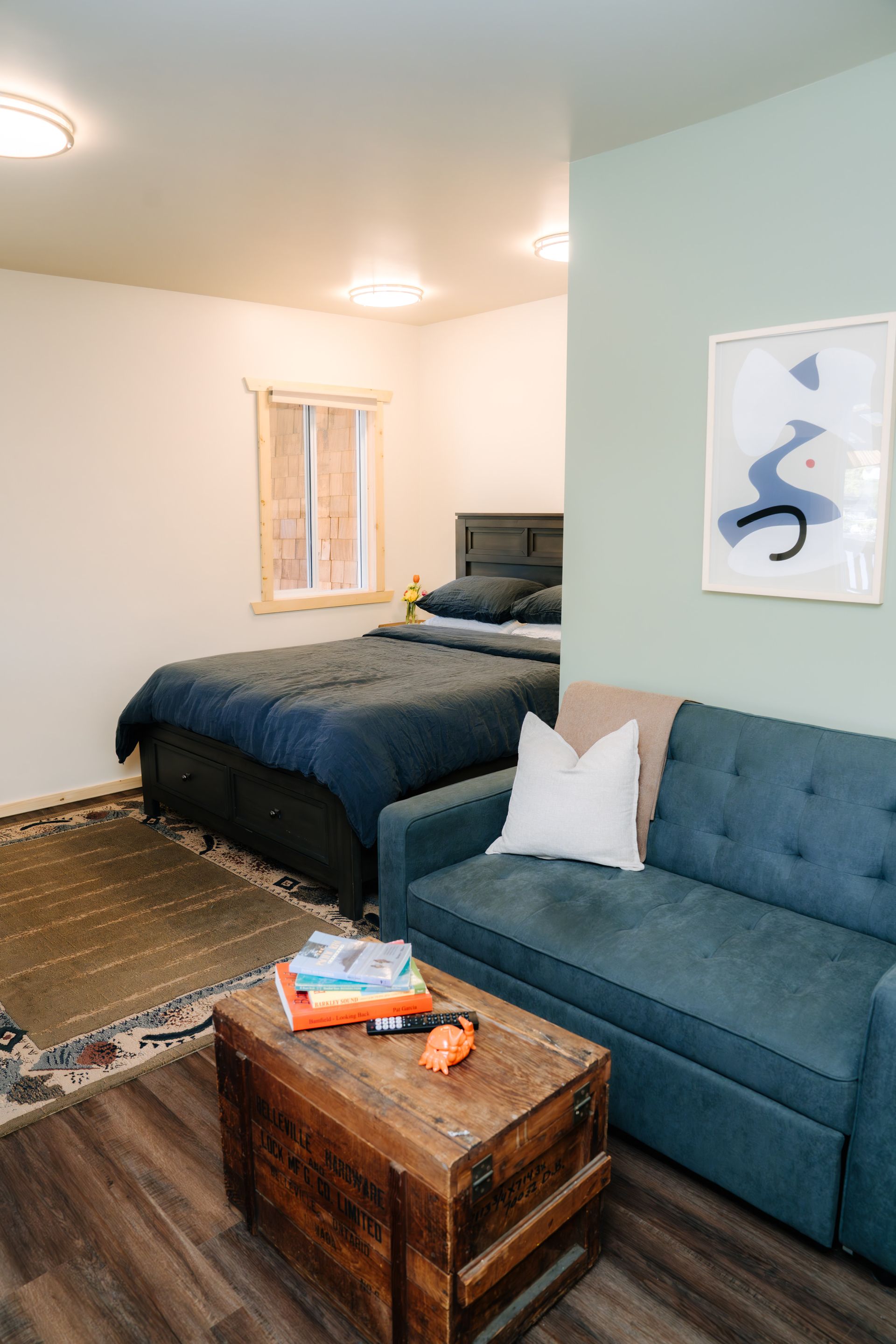 A bedroom featuring a blue bed, a blue tufted sofa with a white pillow, and a rustic wooden trunk coffee table.