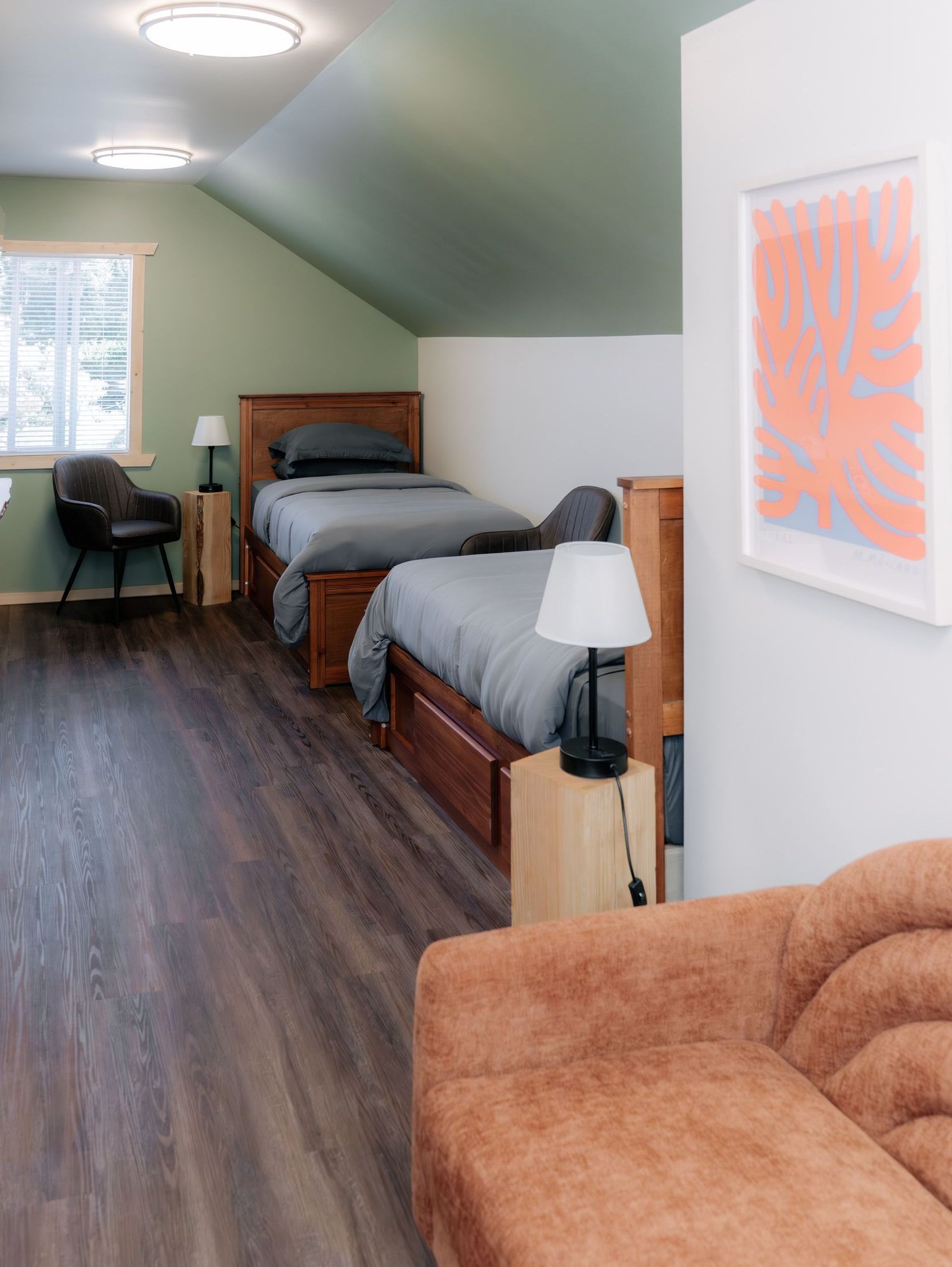 Bedroom with two wooden beds, gray bedding, green slanted walls, dark wood floors, and a textured orange-brown couch.