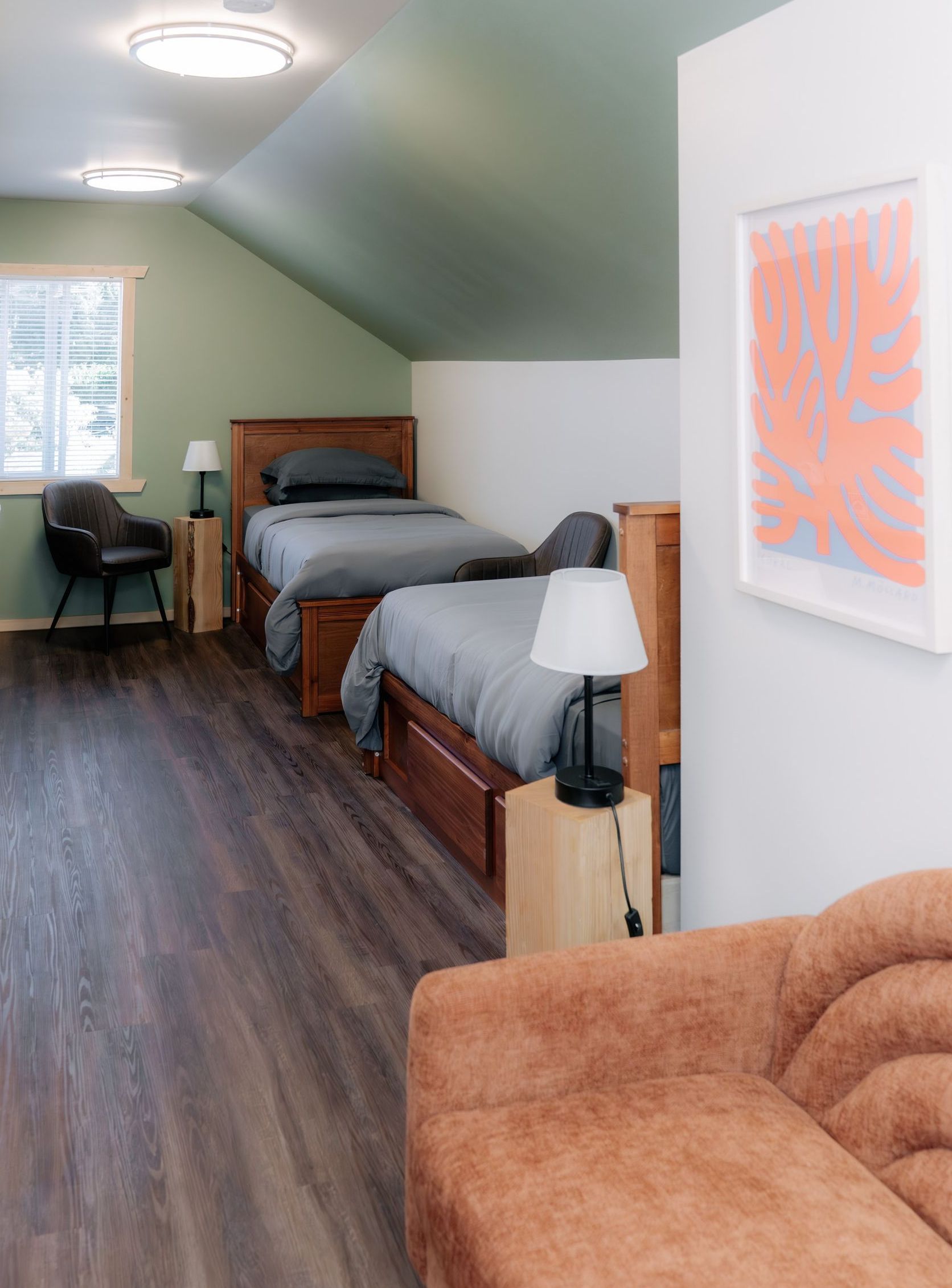 Two twin beds with gray bedding are in a room with green vaulted ceilings, wood floors, and a brown sofa in the foreground.