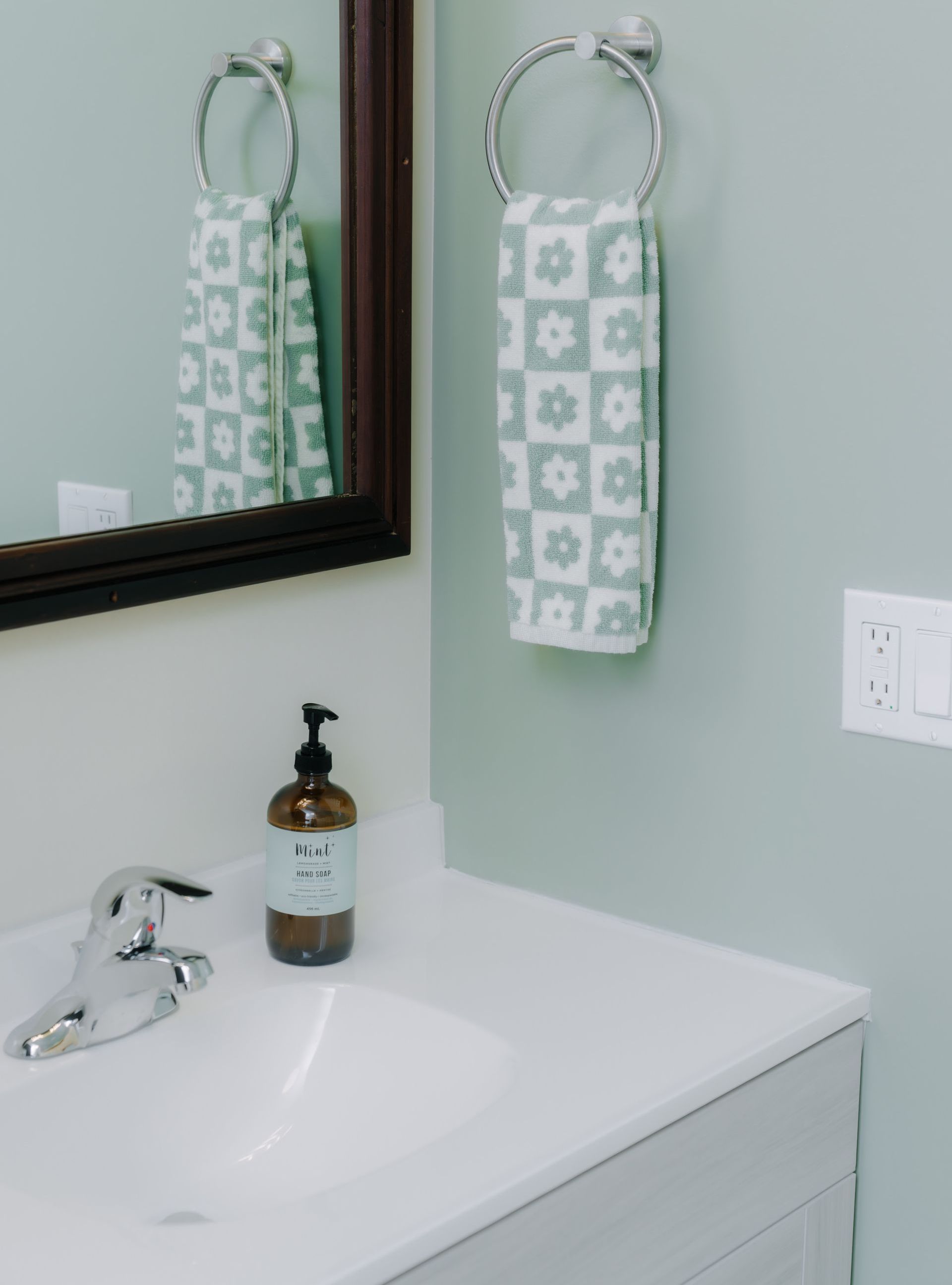 A bathroom vanity with a chrome faucet, a soap dispenser, a wall-mounted towel ring with a floral towel, and a mirror.