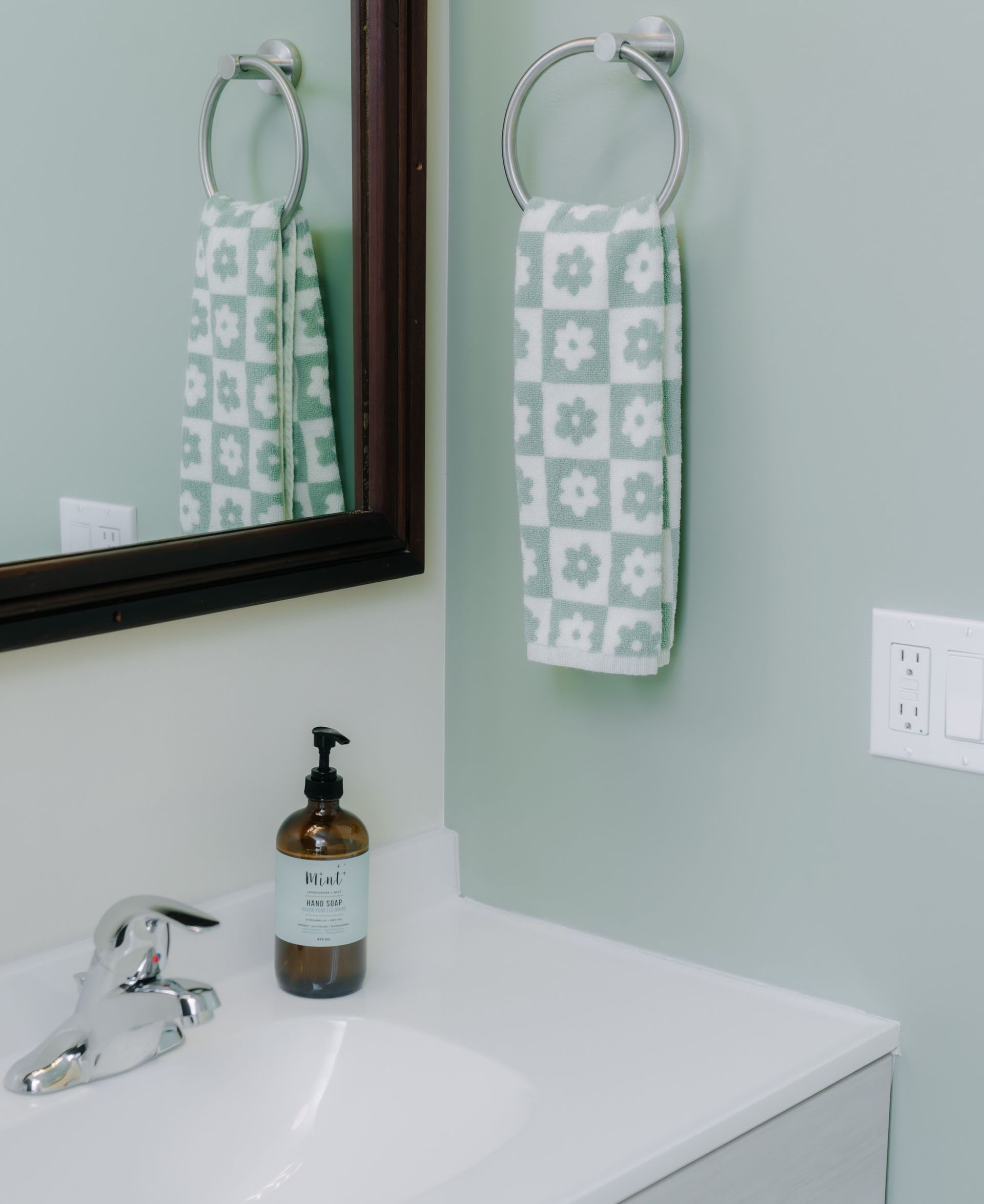 A bathroom vanity with a white sink, soap dispenser, and a patterned hand towel hanging on a wall-mounted ring.