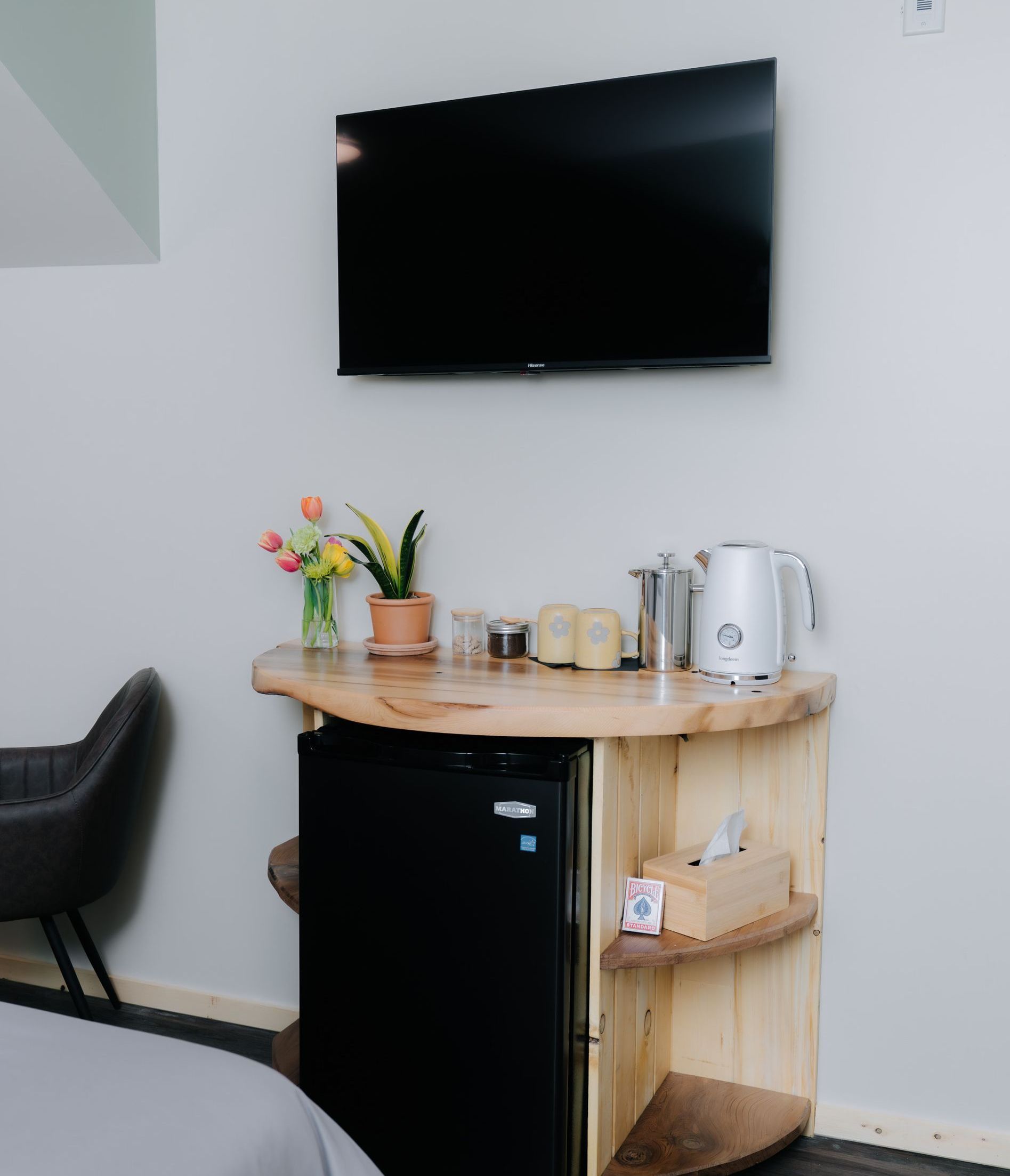 A TV mounted above a custom live-edge wood console holding a small refrigerator, kettle, plants, and a tissue box.
