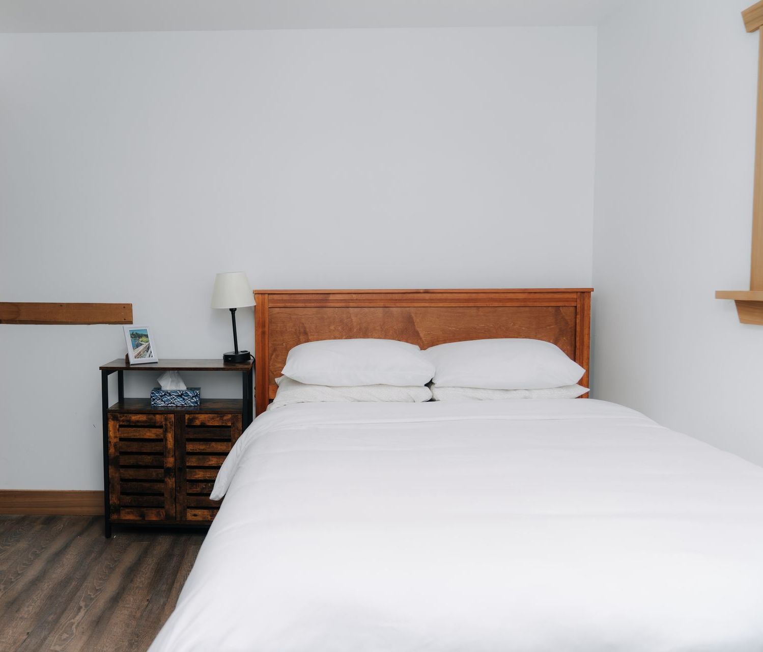 A bedroom with a queen-sized bed featuring white bedding, a wooden headboard, and a bedside table with a lamp.