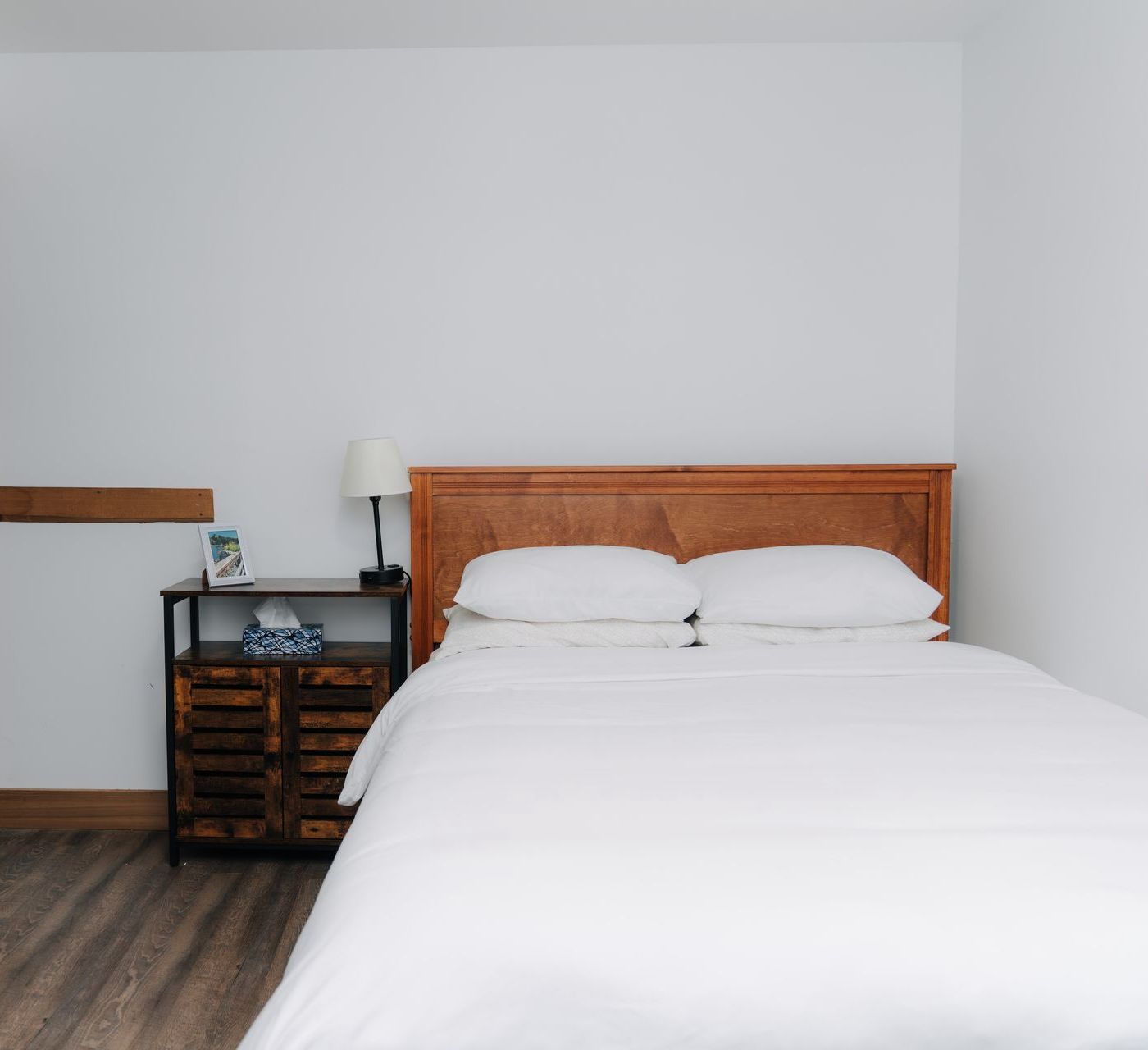 A bedroom with a queen-sized bed covered in white bedding, a wooden headboard, and a rustic wooden nightstand.