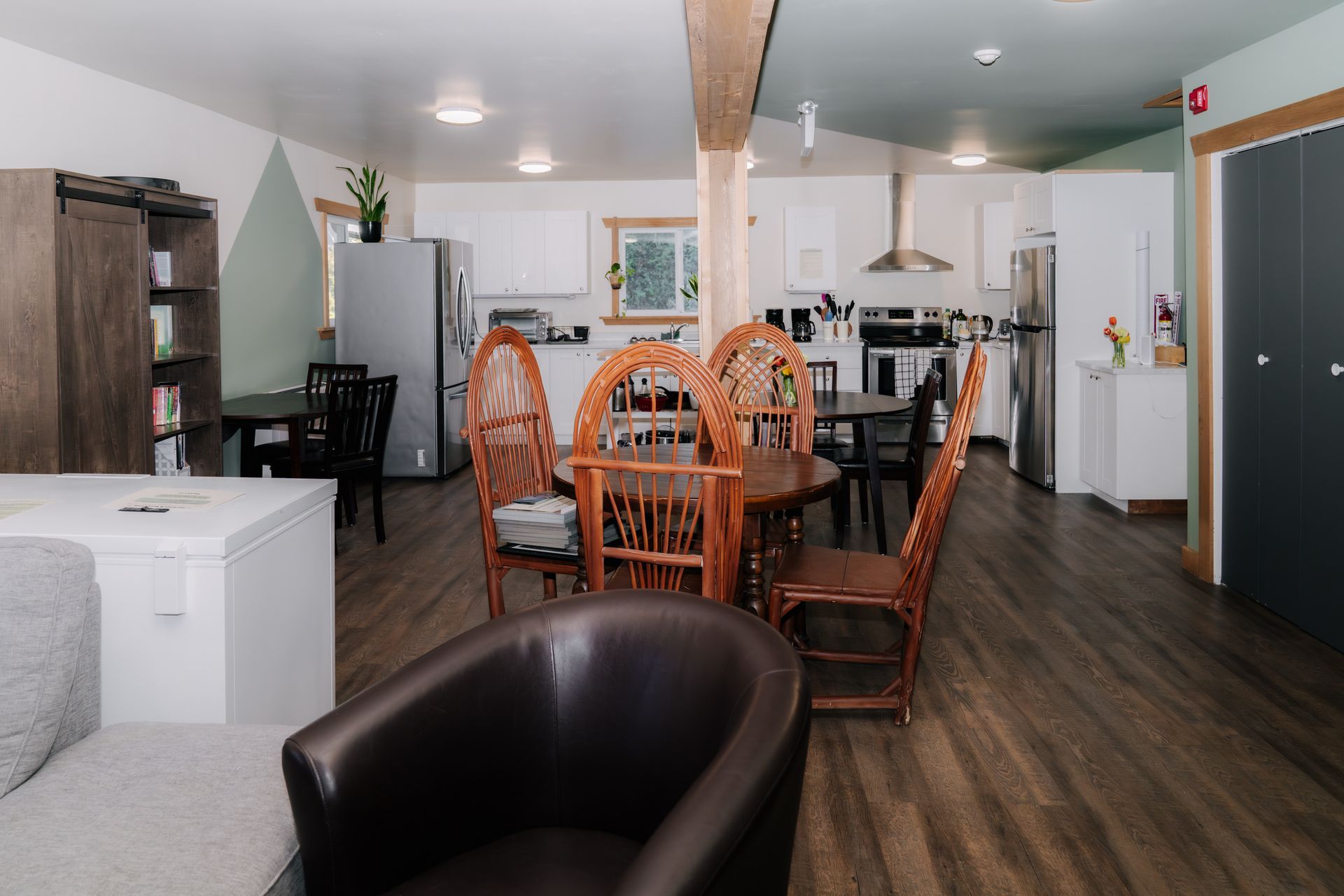 A dining area with a round wood table and wicker-back chairs, viewed from a living space with a leather chair.