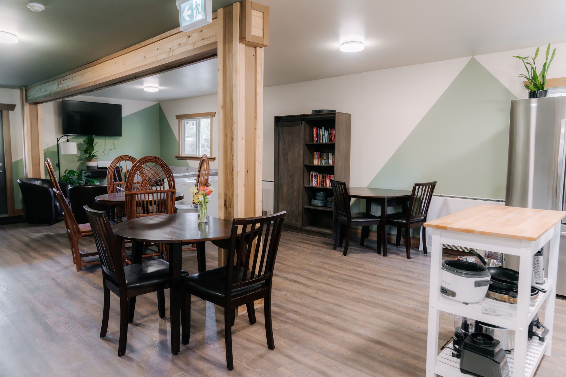 A dining area with a wood-trimmed room divider, two tables with chairs, a tall shelf, and a white kitchen island.