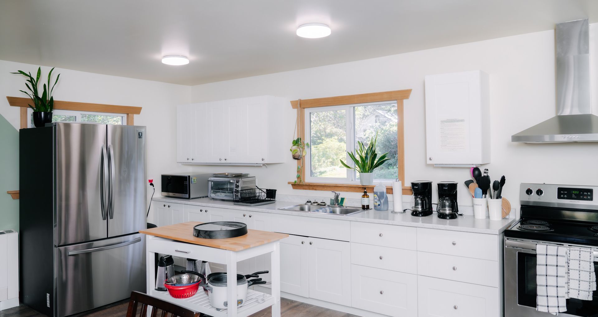 A bright, modern kitchen featuring white cabinets, stainless steel appliances, a wooden kitchen island, and two windows.