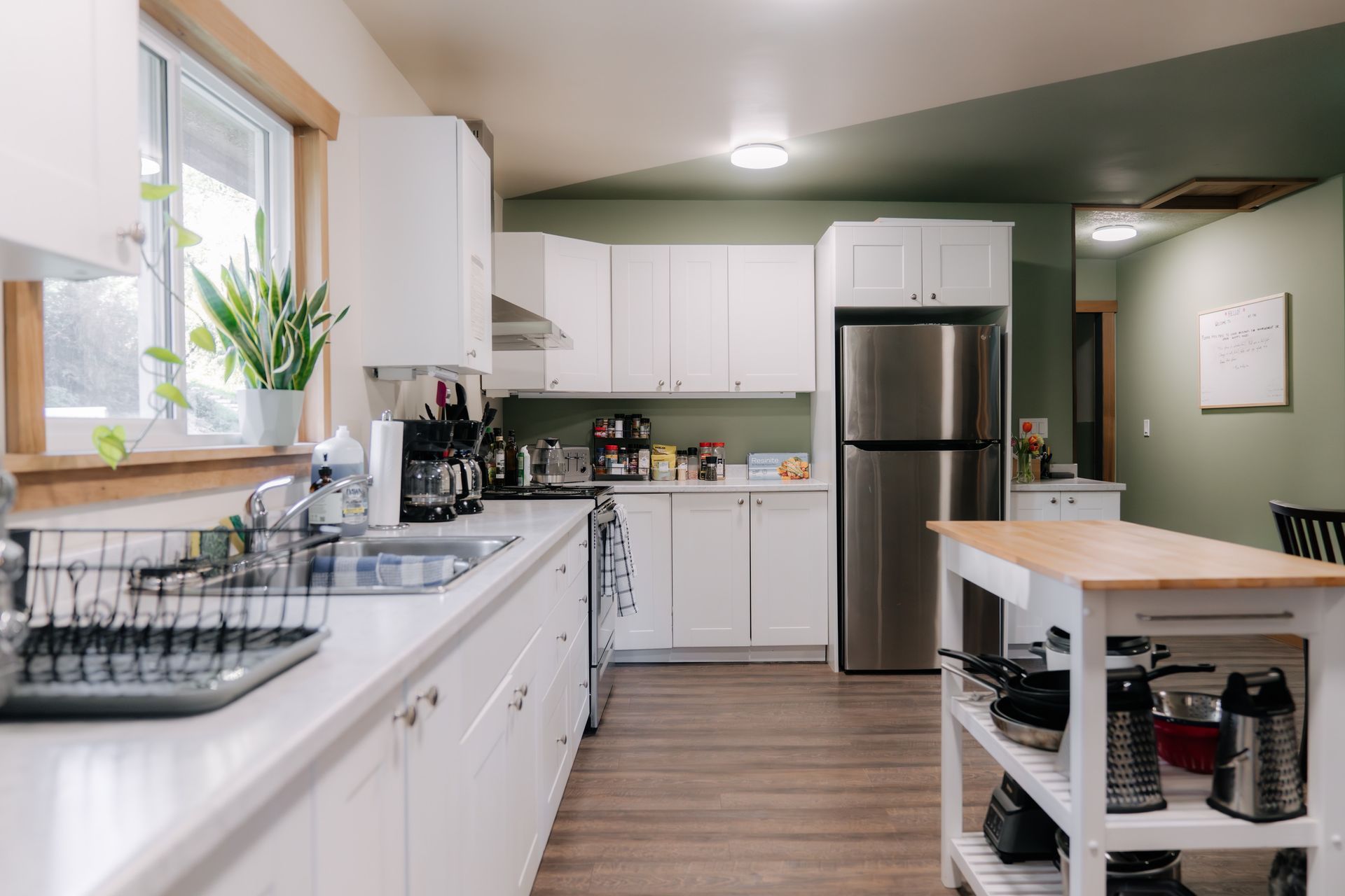 A modern kitchen with white cabinets, light countertops, a stainless steel refrigerator, and a rolling kitchen island.