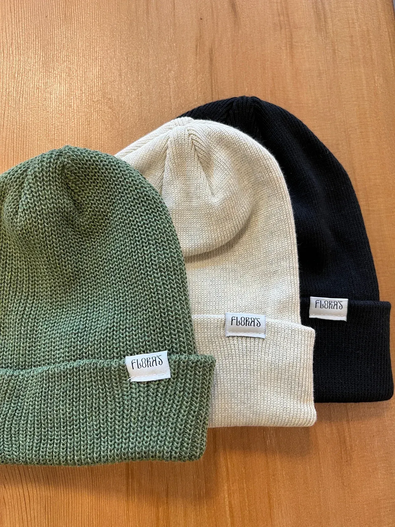 Three beanies are stacked on top of each other on a wooden table.