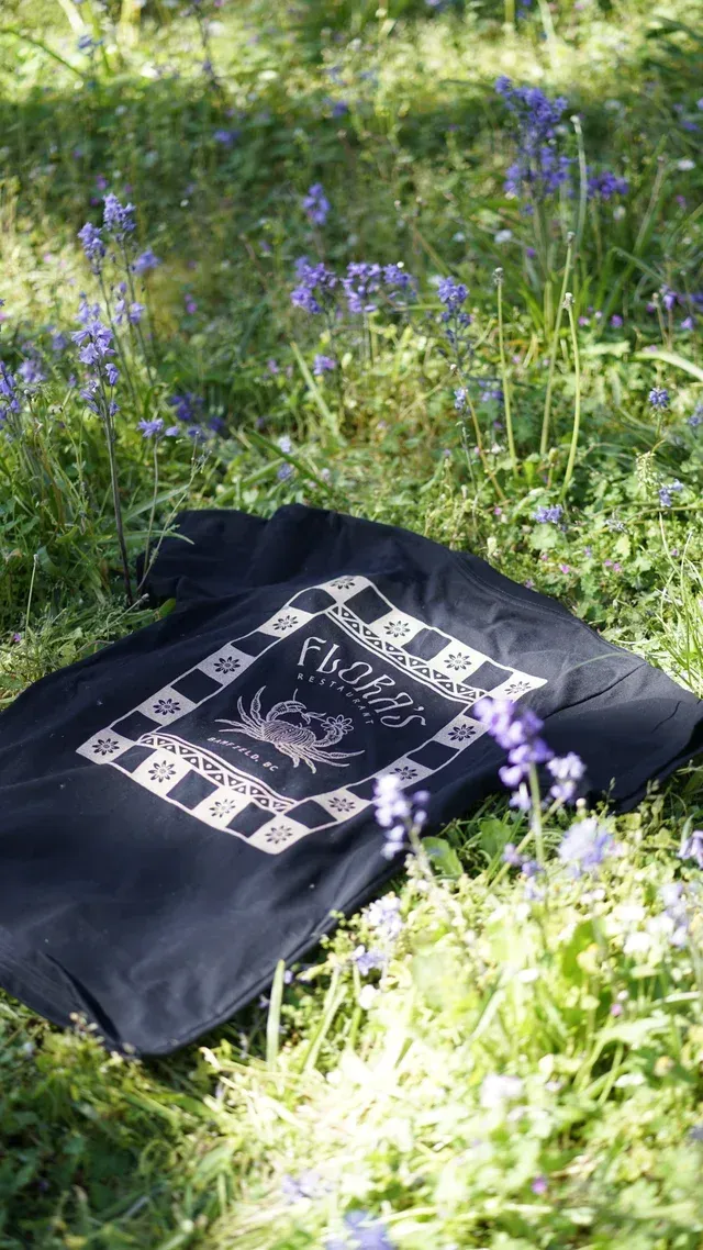 A black t-shirt is laying in the grass surrounded by bluebells.