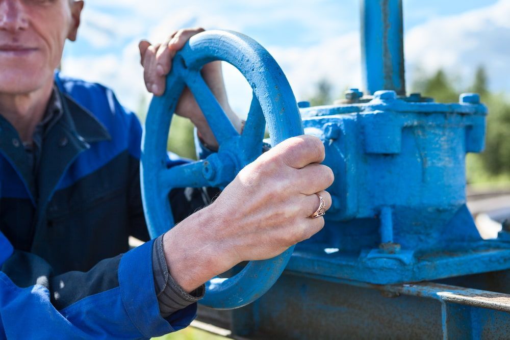 Man in Blue Uniform Turning a Large Blue Valve Outdoors — Forcequip In Mount Isa, QLD