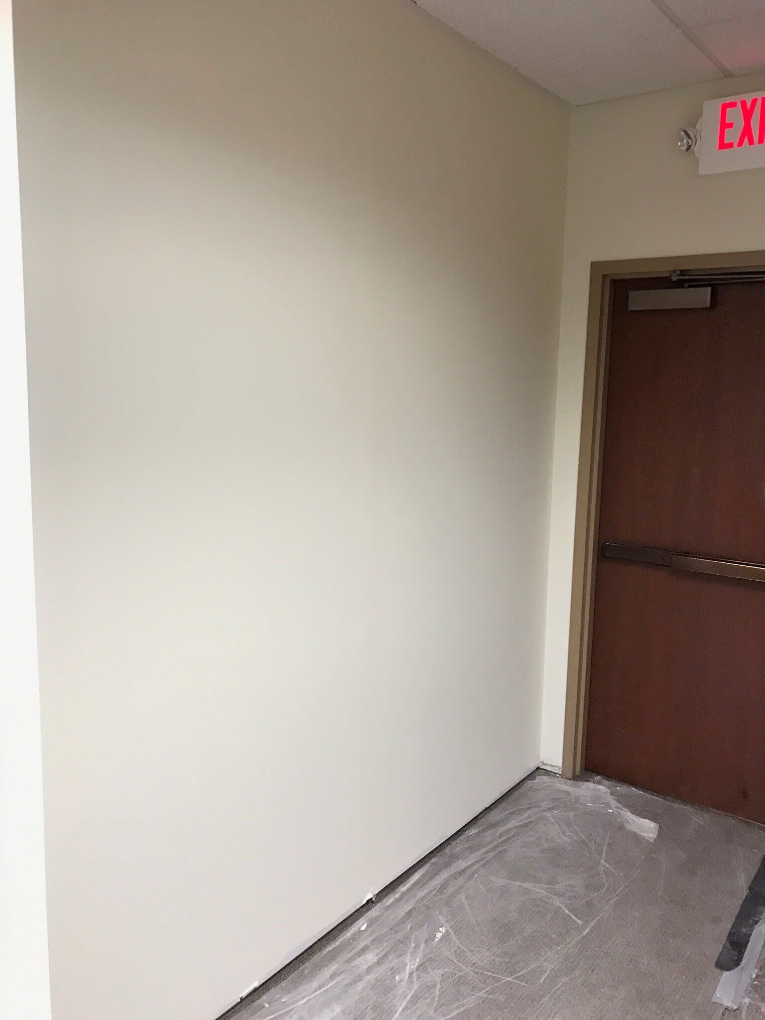A hallway with white walls and a red exit sign.