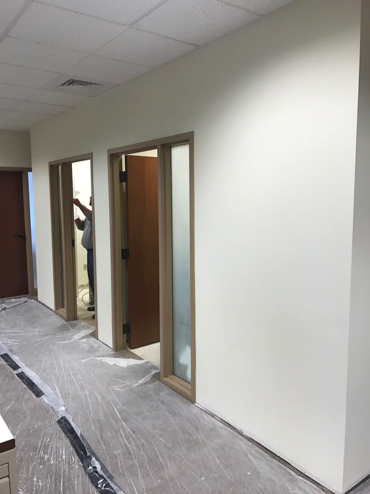A man is standing in a hallway with white walls and wooden doors.
