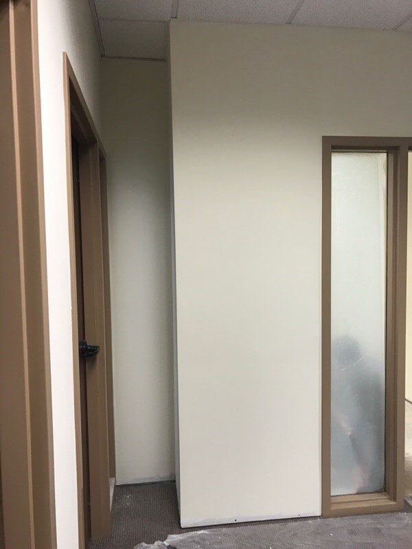 A hallway with a white wall and a glass door