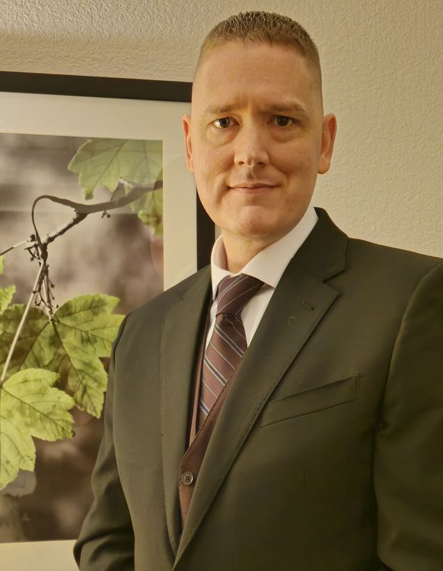 A man in a suit and tie is standing in front of a picture