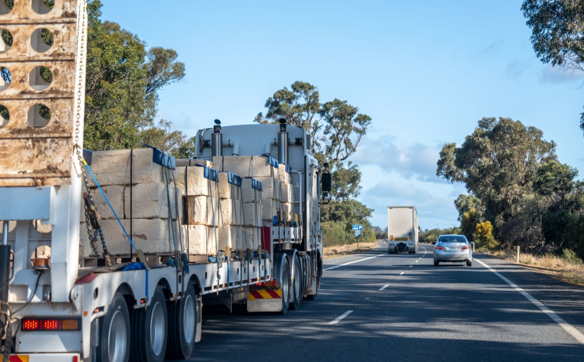 Semi-truck hauling cargo on a highway under a bright blue sky. Other vehicles are also on the road.