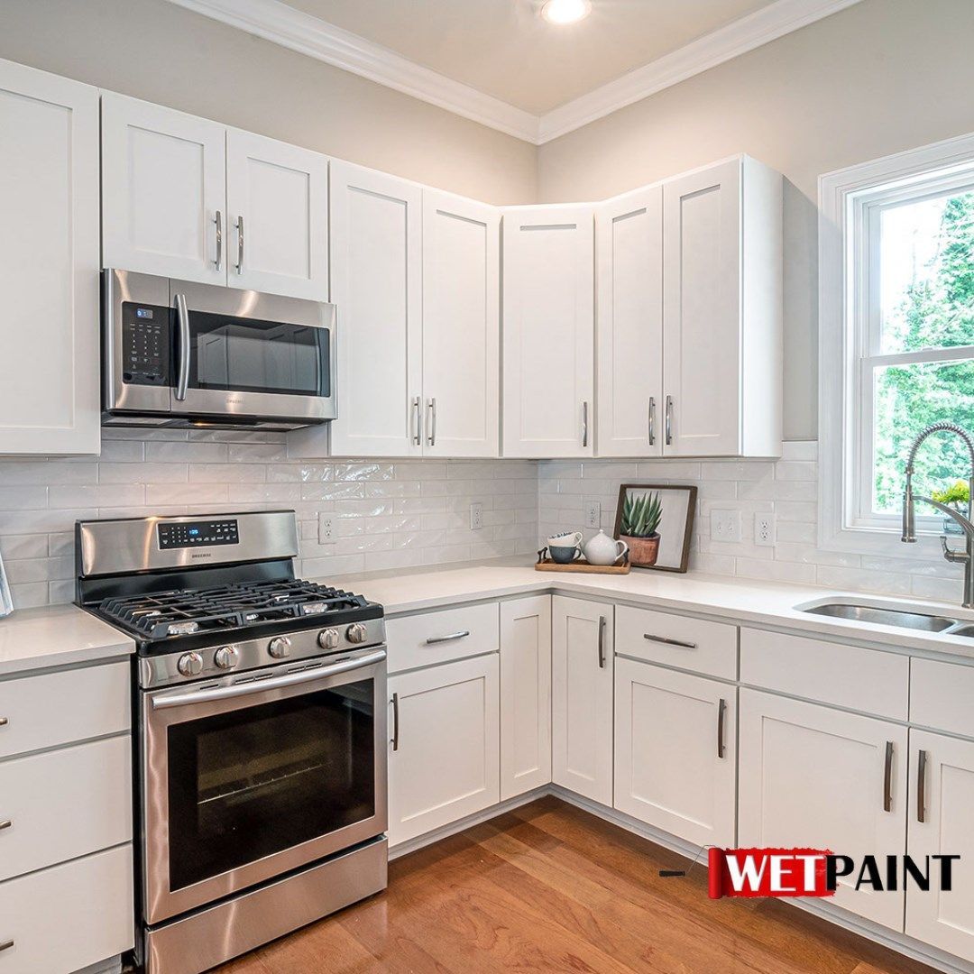 A kitchen with white cabinets , a stove , a microwave , and a sink.
