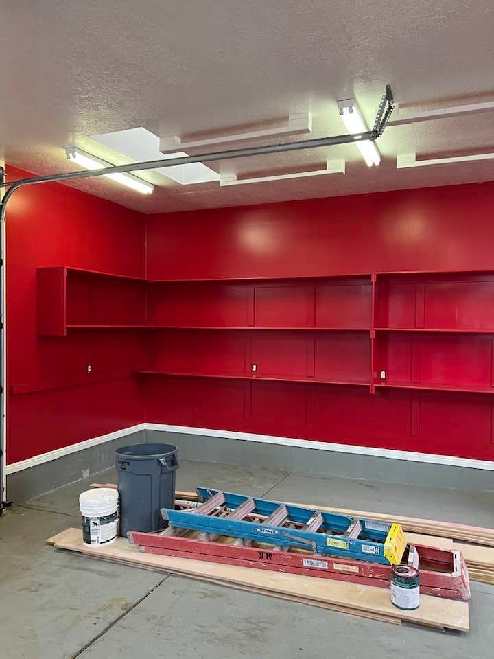 A garage with red walls and shelves and a ladder on the floor.