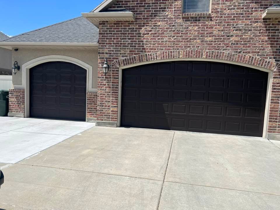 There are two garage doors on the side of a brick house.