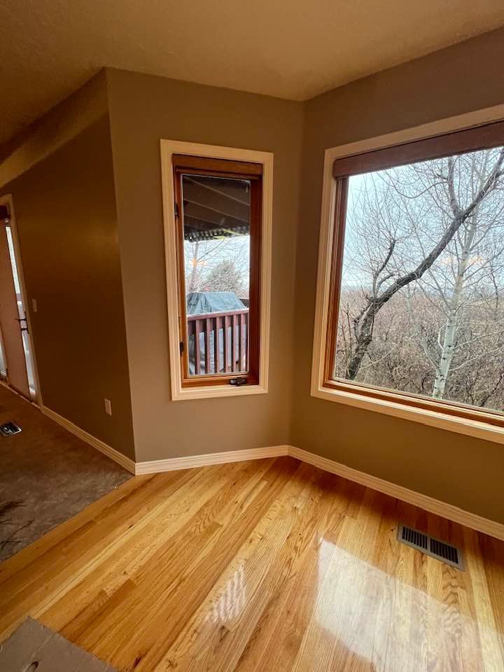 An empty room with hardwood floors and two windows.