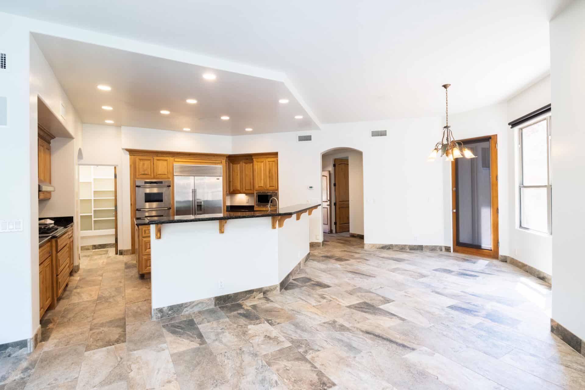 A large empty room with a kitchen , dining room , and living room.