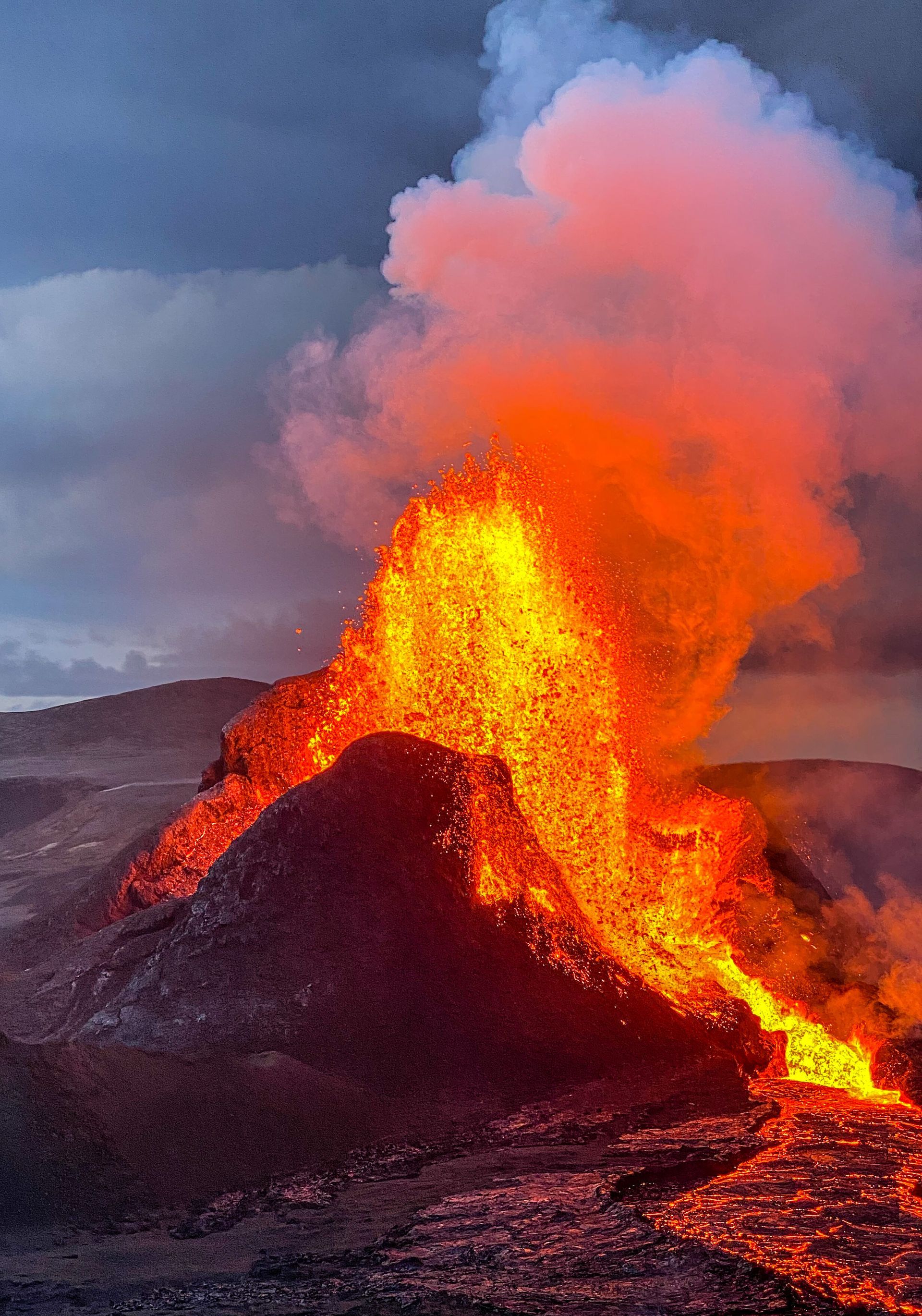 A big volcanic crater gushing lava into the air with dark clouds in the background, framing glowing pink smoke.