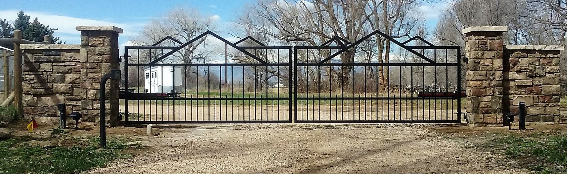 A wrought iron gate is surrounded by stone pillars on a dirt road.