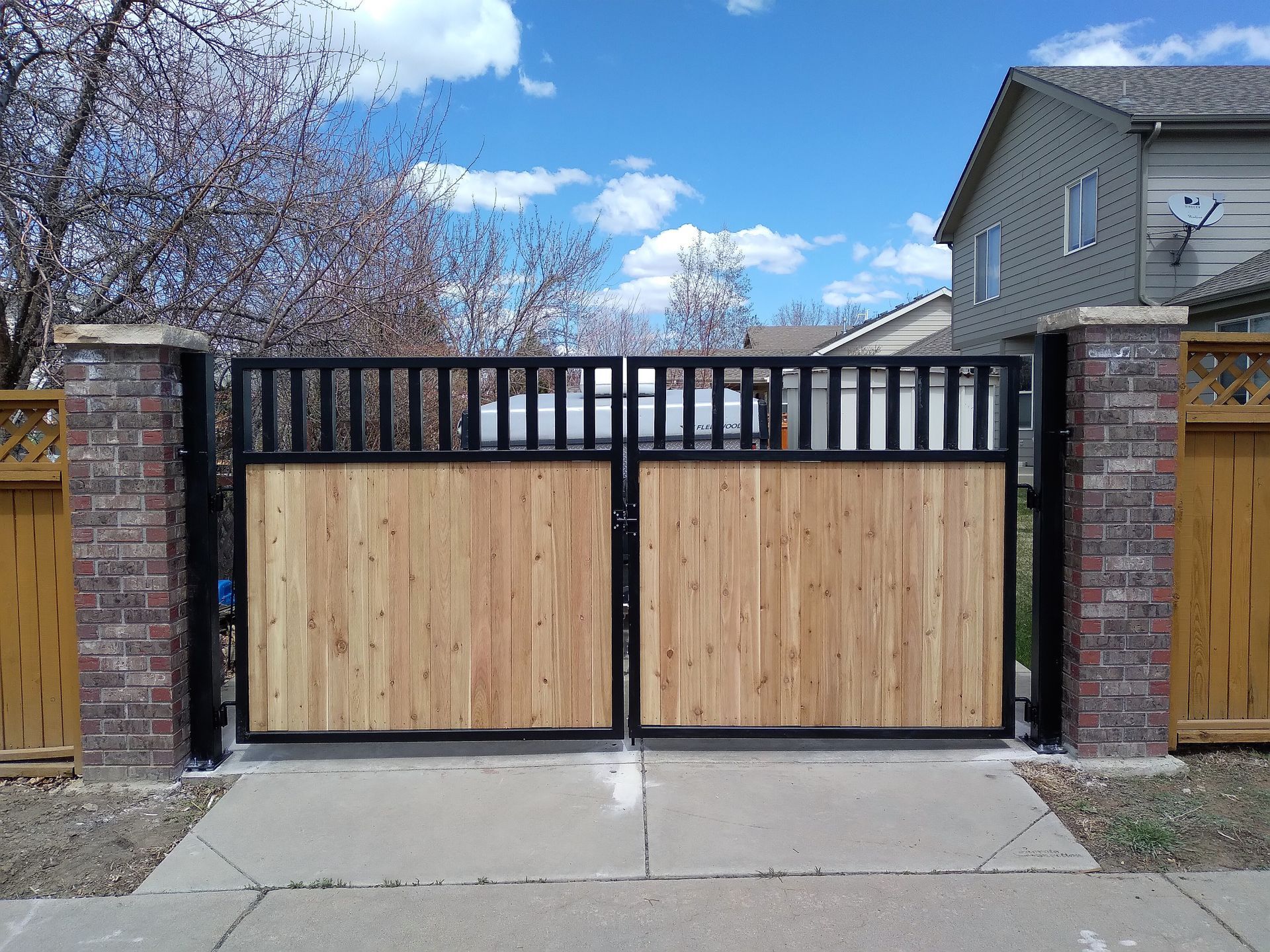A wooden gate is surrounded by brick pillars in front of a house