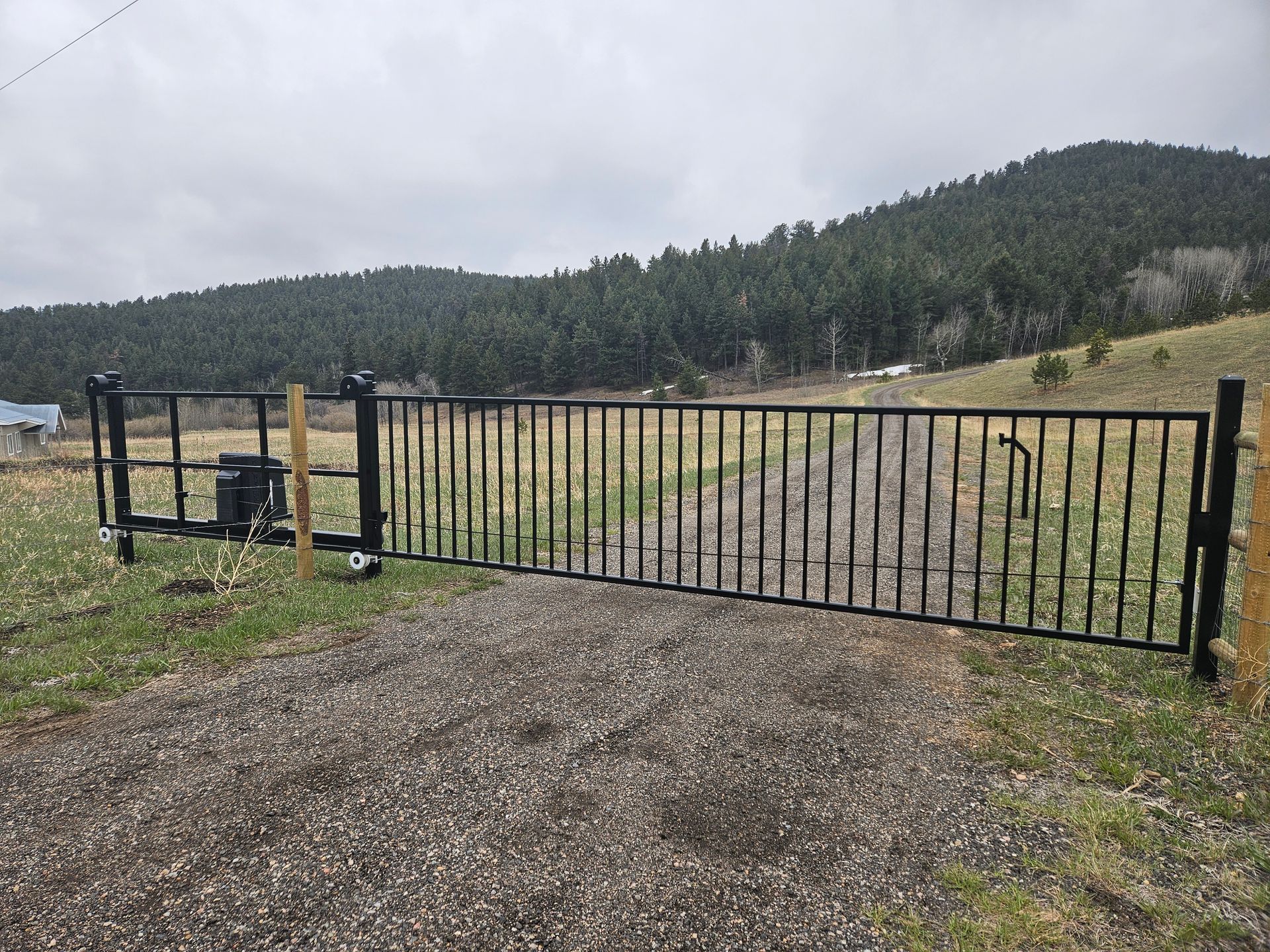 A metal gate is sitting on the side of a gravel road.