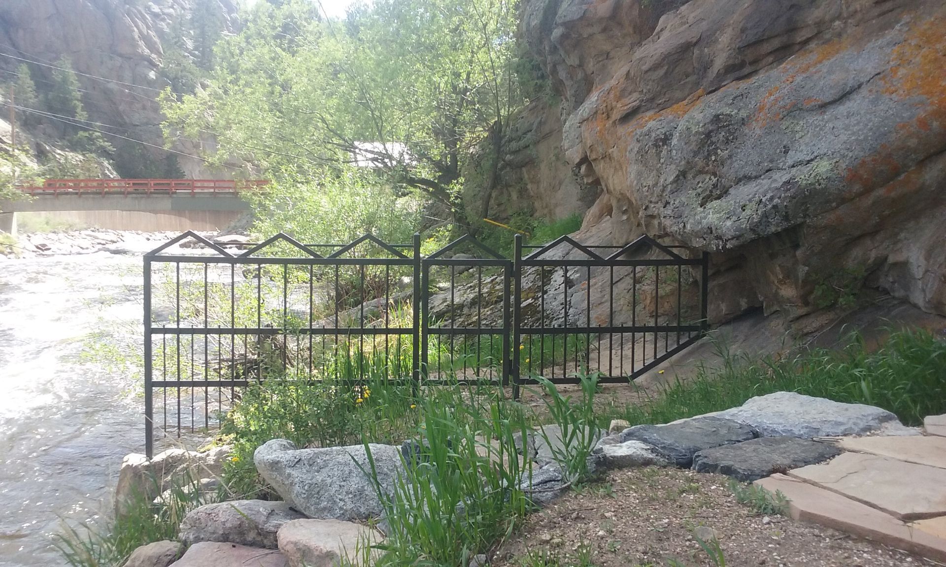 A metal fence is surrounded by rocks and grass next to a river.