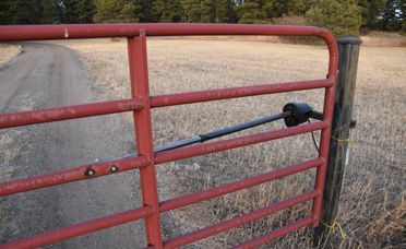 A red gate is open to a dirt road.