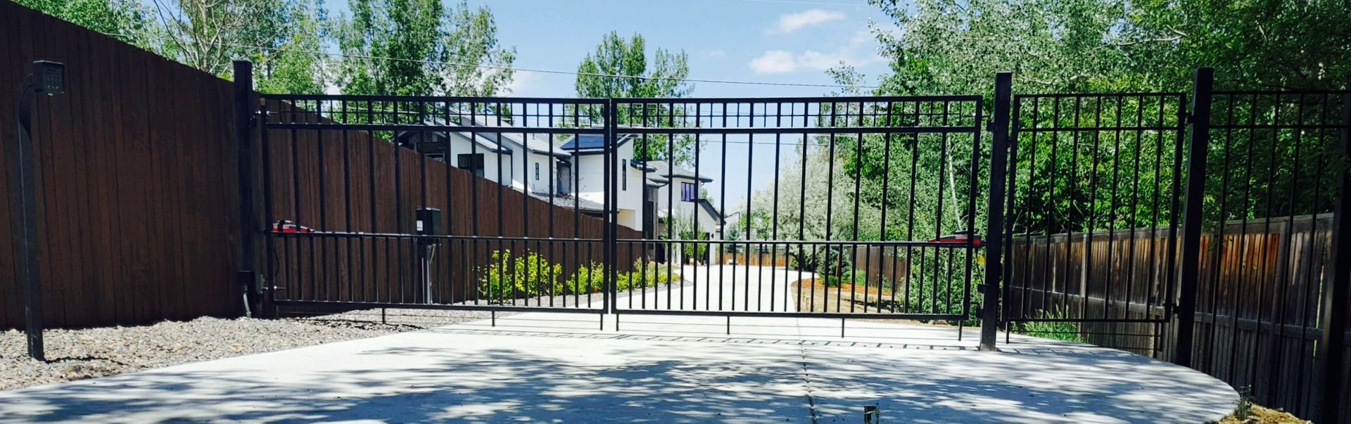 A black wrought iron gate is open to a driveway.