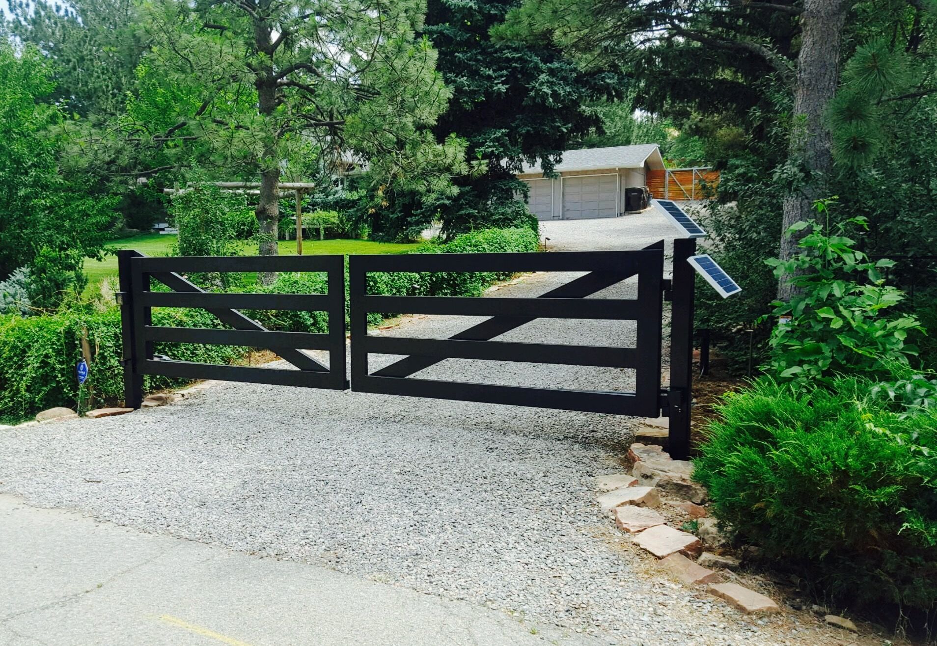 A black wooden gate is open to a gravel driveway