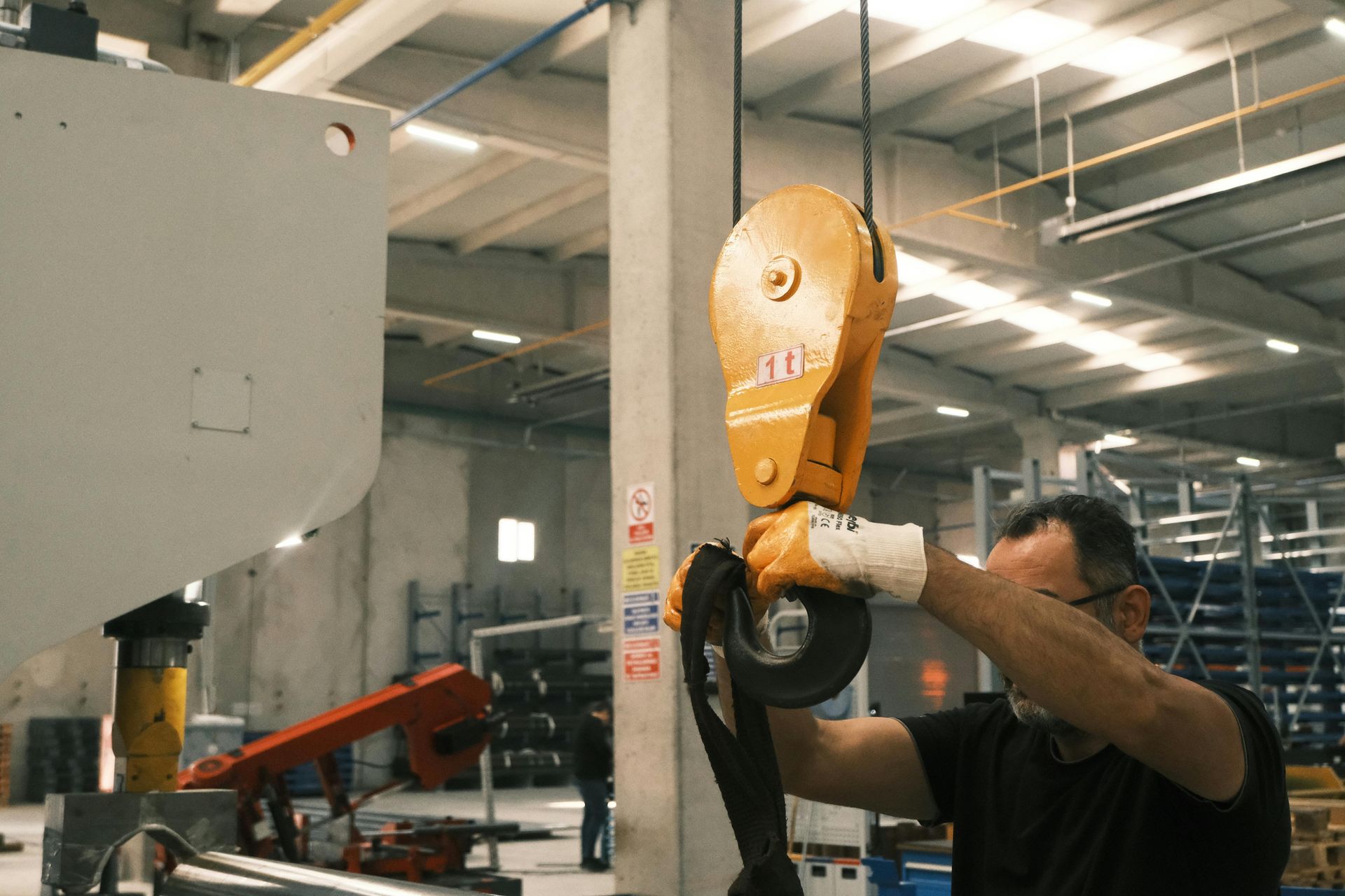 A man is holding a crane hook in a factory.