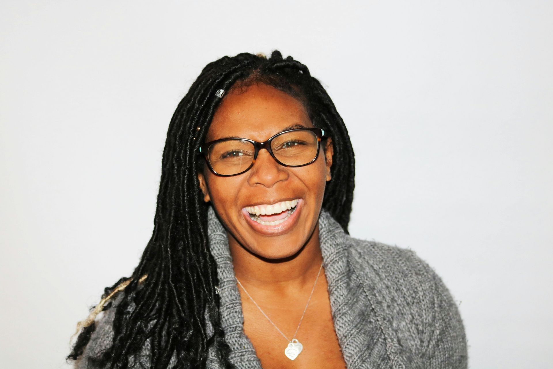 A woman with dreadlocks and glasses is smiling for the camera.