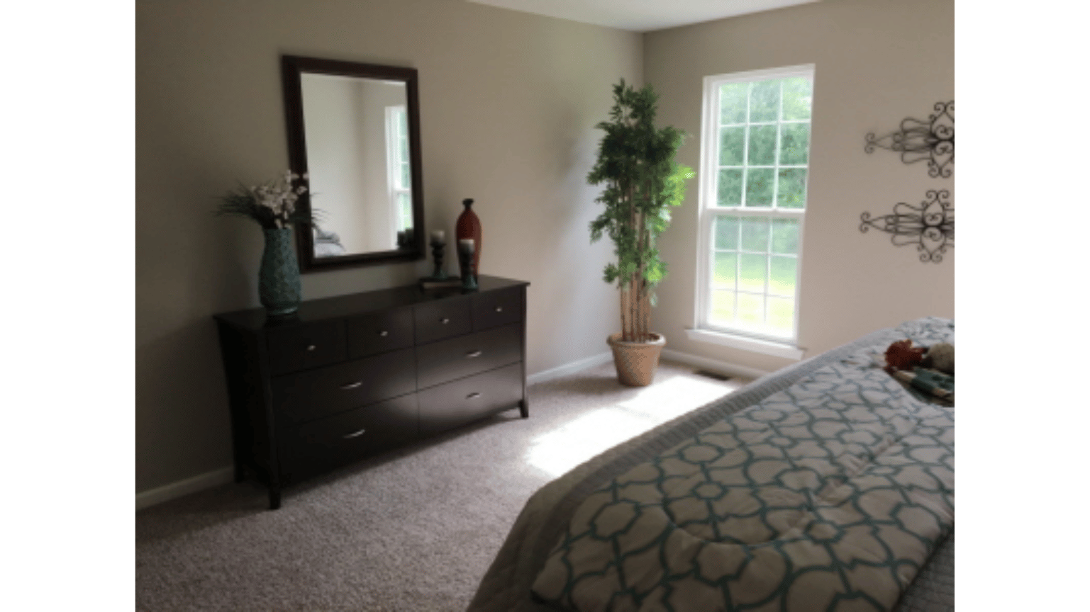 A bedroom with a bed , dresser , mirror and window