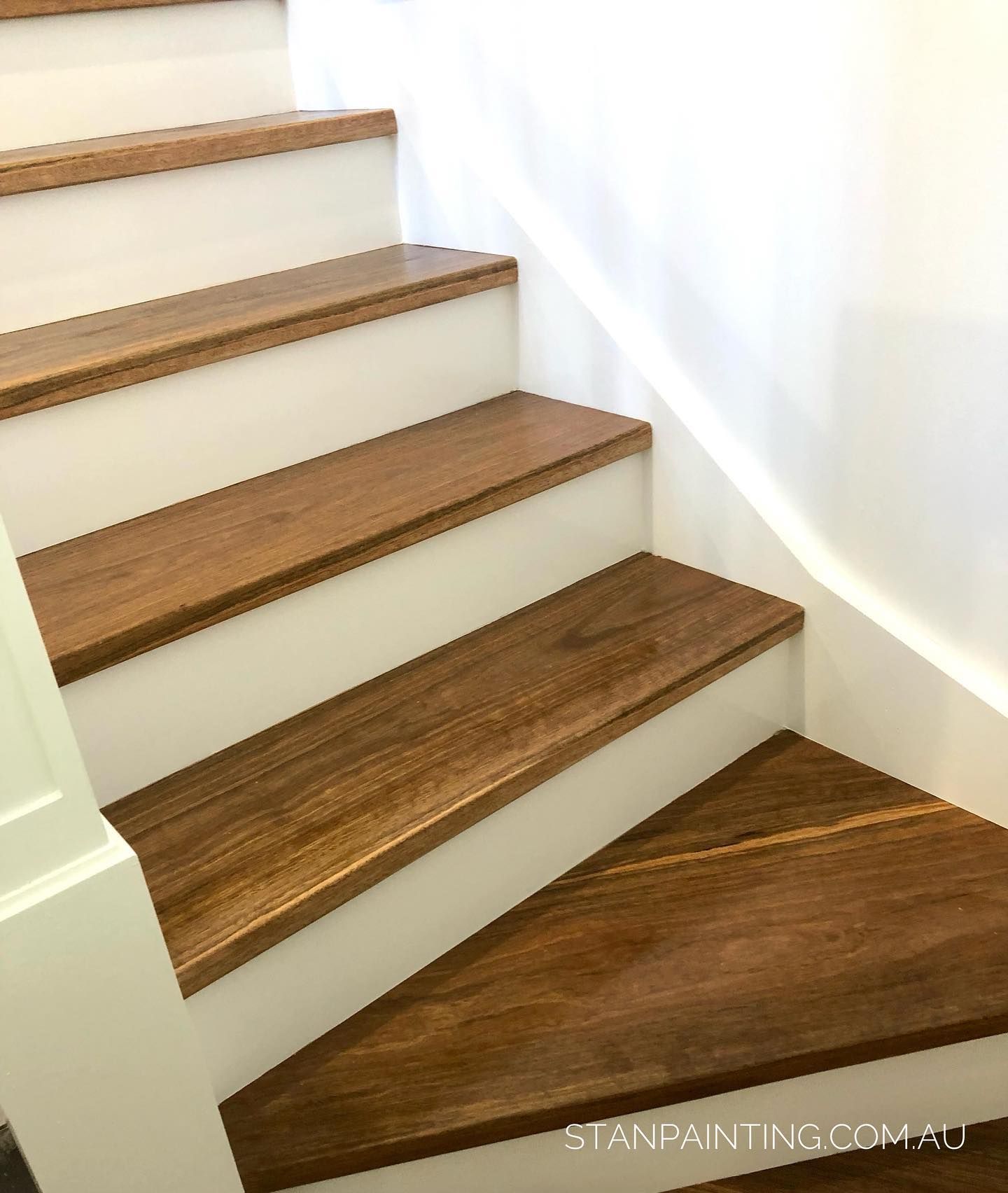 Wooden stair treads with white risers and trim, ascending against a white wall — Stan Painting Services In Thornton, NSW