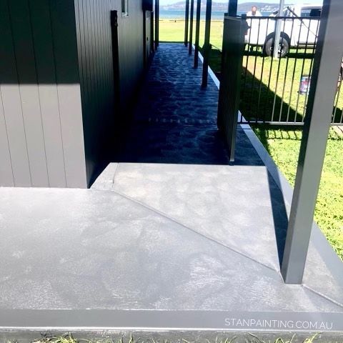 Gray Painted Concrete Patio with Black Fence and Building on A Sunny Day — Stan Painting Services In New Lambton, NSW
