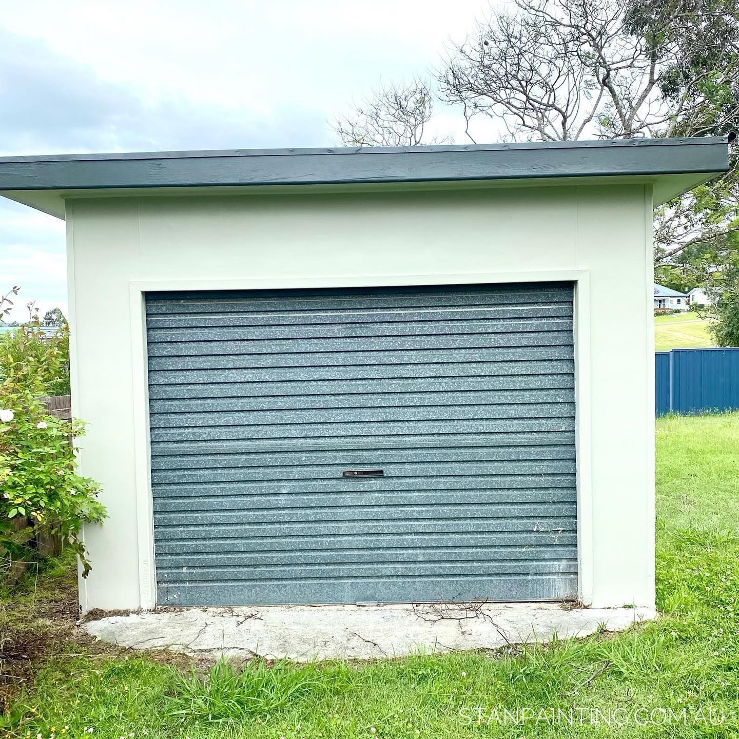 A Small, Light Green Garage with A Gray Metal Roll-Up Door — Stan Painting Services In Newcastle, NSW