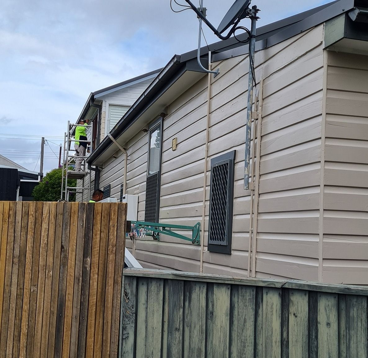 House with Tan Siding, Black Roof, and A Worker on Scaffolding — Stan Painting Services In Kurri Kurri, NSW