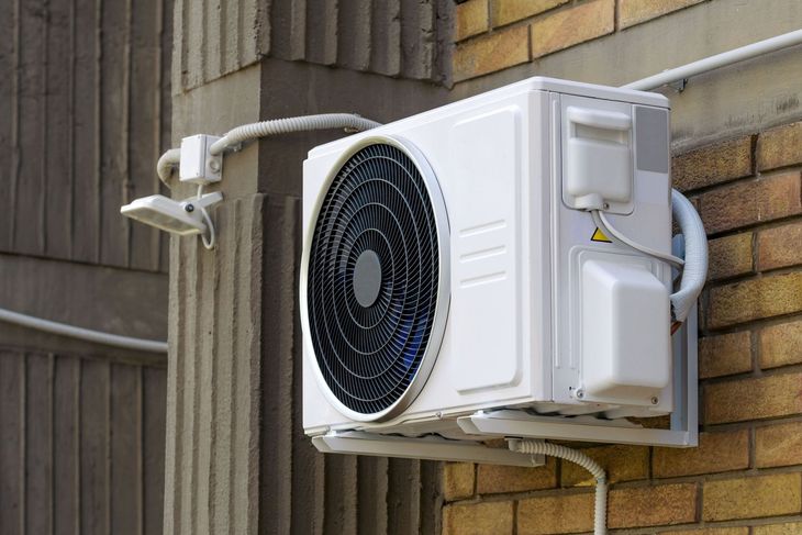 Outdoor air conditioning unit mounted on a brick wall beside a wooden fence