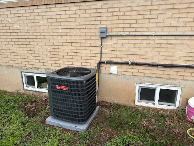 Outdoor HVAC unit beside a brick house, with basement windows and utility lines visible.