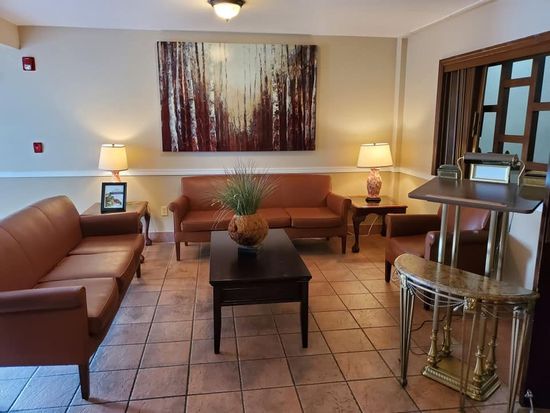 Lounge with brown leather couches, coffee table, lamps, artwork, and a decorative table. Beige walls and tiled floor.