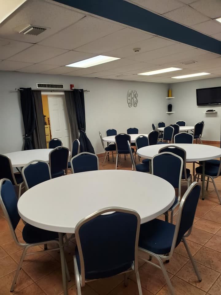 Round tables with blue chairs in a room with a TV and a doorway.