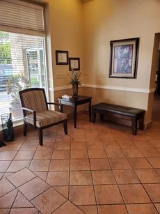 Reception area with chair, table, and bench. Window to the left, framed art on the wall.