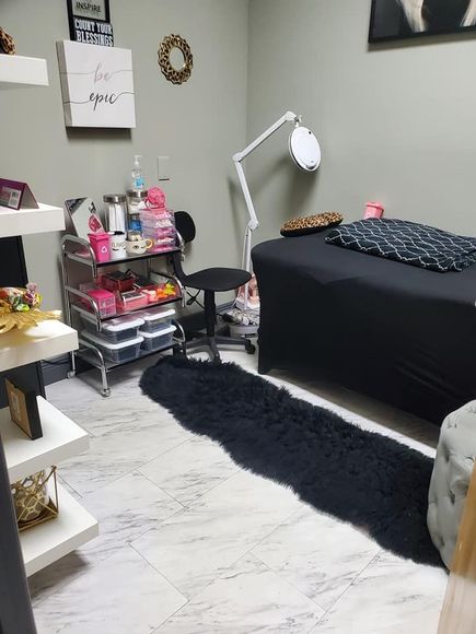 A salon interior with a treatment bed, supplies, and storage, with a black rug and white shelves.