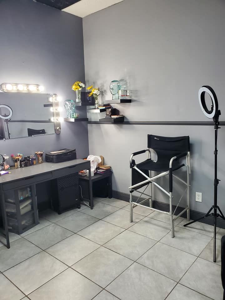 Makeup studio with a desk, mirror, shelves with products, ring light, and a director's chair.