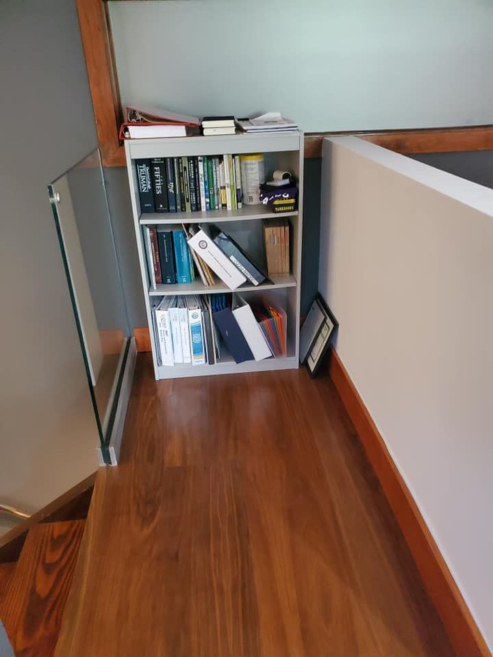 Bookshelf on a wooden floor landing, beside a staircase. Grey walls and glass railing.